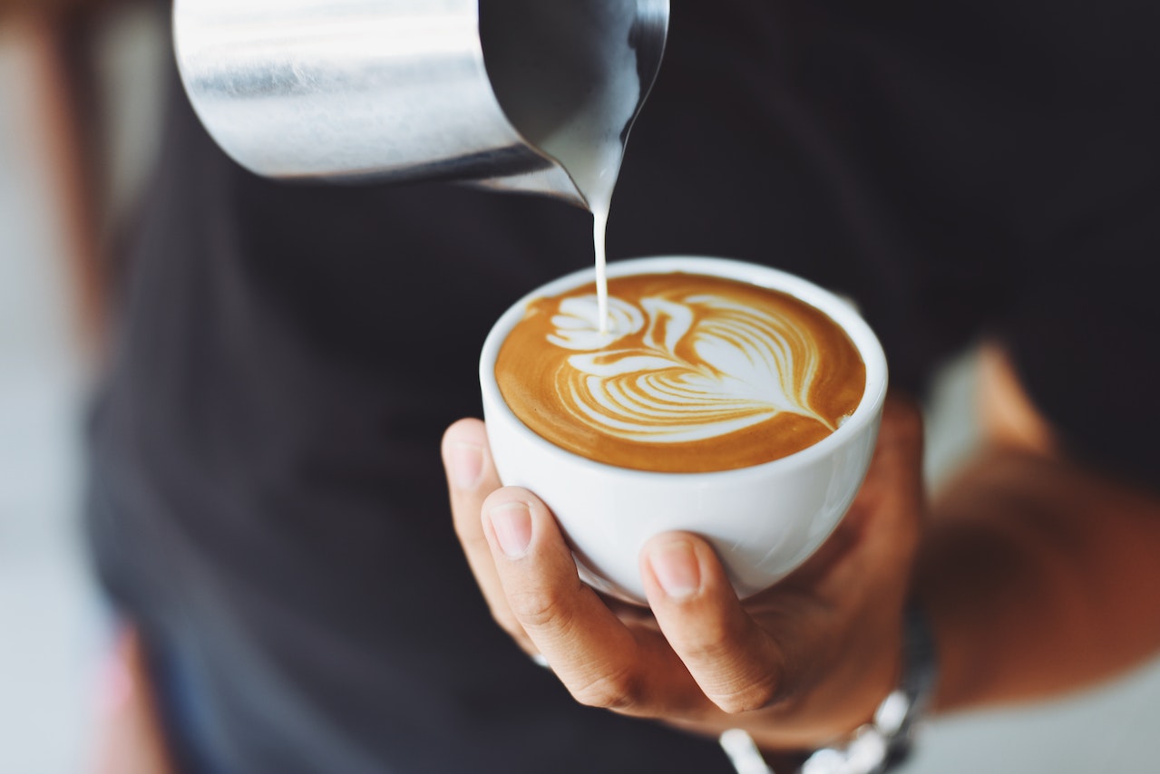 image of a hand holding a cup of coffee and pouring milk into it